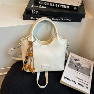Detail view of cream bucket bag with decorative wooden beads and metal brand plaque