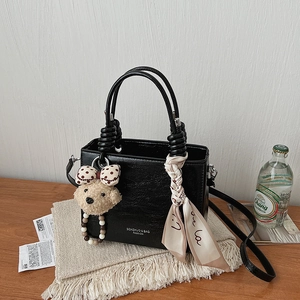 Detail of black textured leather handbag with decorative handles and a plush bear charm