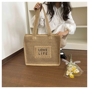 Détail d'un sac cabas en paille tressée avec broderie noire Love Life et poignée