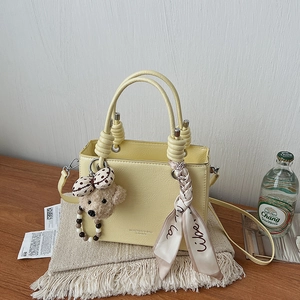 Detail of light yellow textured handbag featuring a scarf handle and a cute bear charm