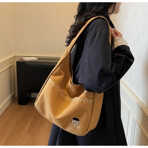 Detail of ginger yellow canvas hobo bag with Docile-girl embroidery and white stitching