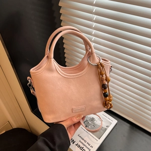 Detail of light pink leather bucket bag with metallic logo and beaded wooden charm