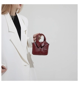 Détail du sac à main bordeaux en cuir en forme de chemise porté sur un blazer blanc élégant