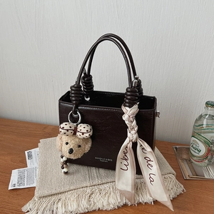 Close-up of structured dark brown mini handbag with knotted handles and plush charm