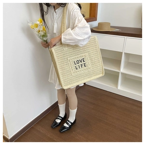 Détail du sac cabas en paille tressée avec écusson LOVE LIFE sur surface beige texturée