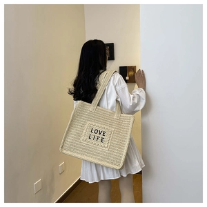Détail d'un sac cabas tissé beige avec texte LOVE LIFE porté à l'épaule d'un mannequin