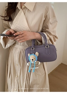 Detail view of a purple vintage shoulder bag with a cute plush bear charm on a beige coat