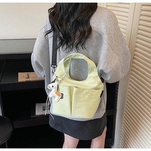 Détail du sac fourre-tout en toile vert clair avec deux poches avant et bandoulière réglable