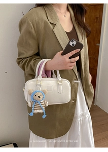 Detailed view of white Boston handbag with embossed logo and cute teddy bear charm accessory