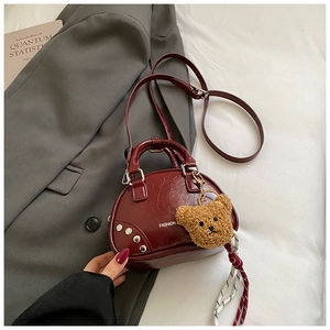 Détail du sac coquille bordeaux avec rivets argentés et texte fashion sur le cuir