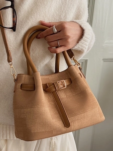 Brown woven texture handbag with leather straps and gold buckle shown in a lifestyle view