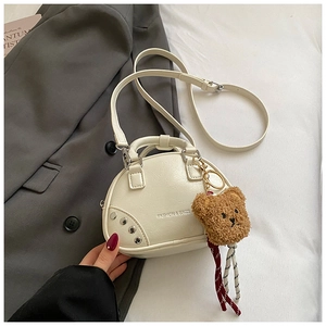 Détail du sac à main crème en cuir avec rivets argentés et pendentif ours en peluche