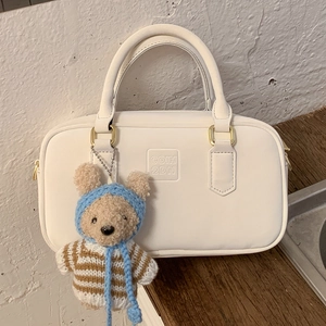 Close-up of off-white faux leather handbag with logo embossing and teddy bear charm