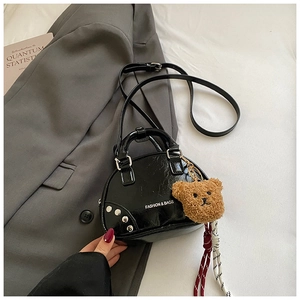 Détail du sac coquille en cuir verni noir avec rivets et breloque ours sur un costume gris