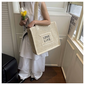 Détail d'un sac cabas tissé beige avec écusson noir Love Life dans une pièce lumineuse