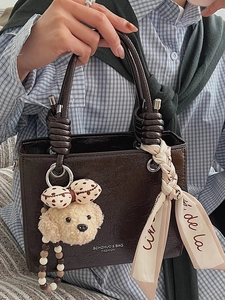Dark brown glossy handbag with twist handle, teddy bear charm, and silk scarf detail