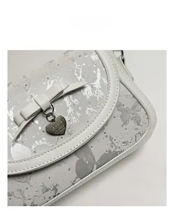 Détail d'un sac à main en cuir blanc avec imprimé papillon et pendentif coeur en métal