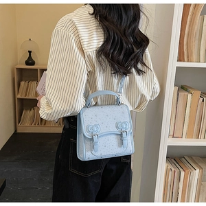 Close-up of a light blue bow backpack with silver star prints and pin buckle detail