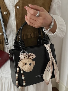 Minimalist black leather handbag with pearl chain and silk scarf shown in a lifestyle shot