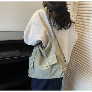 Detail of sage green nylon crossbody bag with large front flap pockets and wide strap