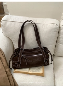 Detail of dark brown canvas tote bag with contrast stitching and embossed logo on sofa