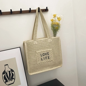 Détail d'un sac cabas tissé beige avec texte Love Life suspendu à un crochet mural