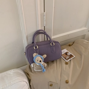 Detail of purple Boston handbag with gold hardware and cute knitted bear charm accessory
