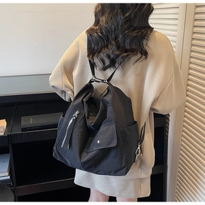 Detail view of black matte nylon tote bag showing side pocket and silver zippers