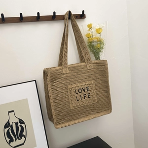Détail d'un sac cabas tissé avec patch LOVE LIFE suspendu sur un mur minimaliste