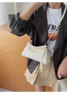 Detail of white leather shoulder bag with ruched closure and golden ring pendant on model