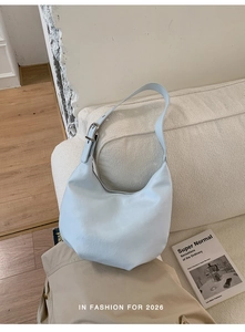 Close-up of a light blue crescent shoulder bag on a minimalist beige fabric sofa