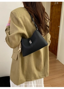 Rear view of a model wearing a black pebbled leather underarm bag with silver twist lock