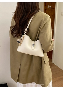 Detail of off-white leather bucket bag with metal clasp and plush pendant on model