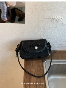Détail du sac à bandoulière noir avec pois blancs, nœud ruban et pendentif cœur argenté
