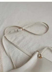 Détail de la bandoulière réglable avec boucle dorée sur un sac minimaliste crème