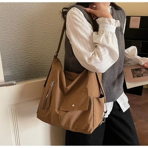 Detail of a large brown canvas tote bag with front flap pocket and functional side pockets