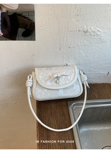 Détail du sac blanc en cuir PU avec nœud pailleté et pendentif cœur argenté sur bois