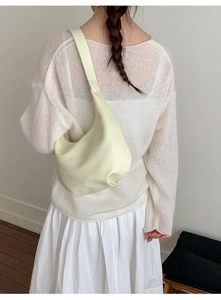Detail of a creamy yellow hobo bag worn by a model in a minimalist outdoor setting