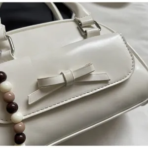 Close-up of white leather handbag featuring a stylish bow and contrast beaded chain
