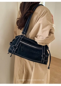 Close-up of black tote bag with white contrast stitching and embossed text on the side