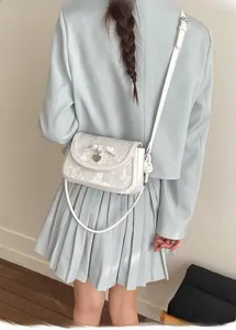 Détail du sac à bandoulière blanc avec nœud papillon et pendentif en forme de cœur