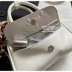 Detailed view of the front flap pocket on a white PU leather handbag with silk scarf charm