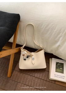 Close-up of beige textured leather bucket bag with silver twist lock and heart pendant