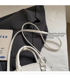 Detail of white leather pillow bag with adjustable strap on a dark gray suit