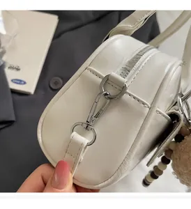 Close-up of white leather handbag showing silver zipper hardware and plush charm detail