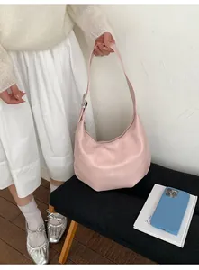 Pink matte leather hobo bag with adjustable strap placed on a black wooden bench