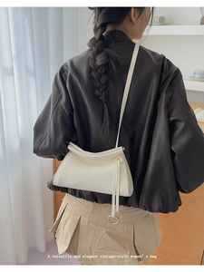 Detail of cream white leather bag showing unique rolled top and long tassel with metal ring