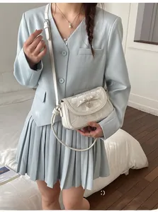 Détail d'un sac bandoulière blanc avec nœud et bandoulière en perles sur un costume bleu