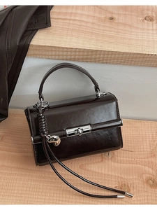 Detail einer dunkelbraunen Lederhandtasche mit silbernem Drehschloss und Herz-Quasten-Anhänger