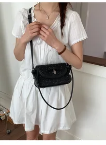 Détail du sac bandoulière noir à pois avec un nœud et un pendentif en forme de cœur